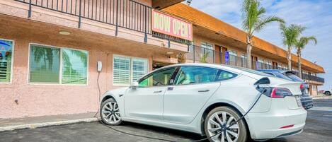 A white Tesla parked in front of a building with a 'NOW OPEN' sign.