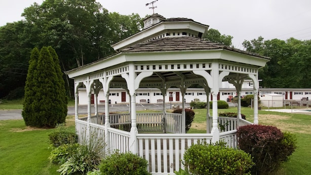 A gazebo with a white picket fence, surrounded by well-maintained grass and various shrubs.