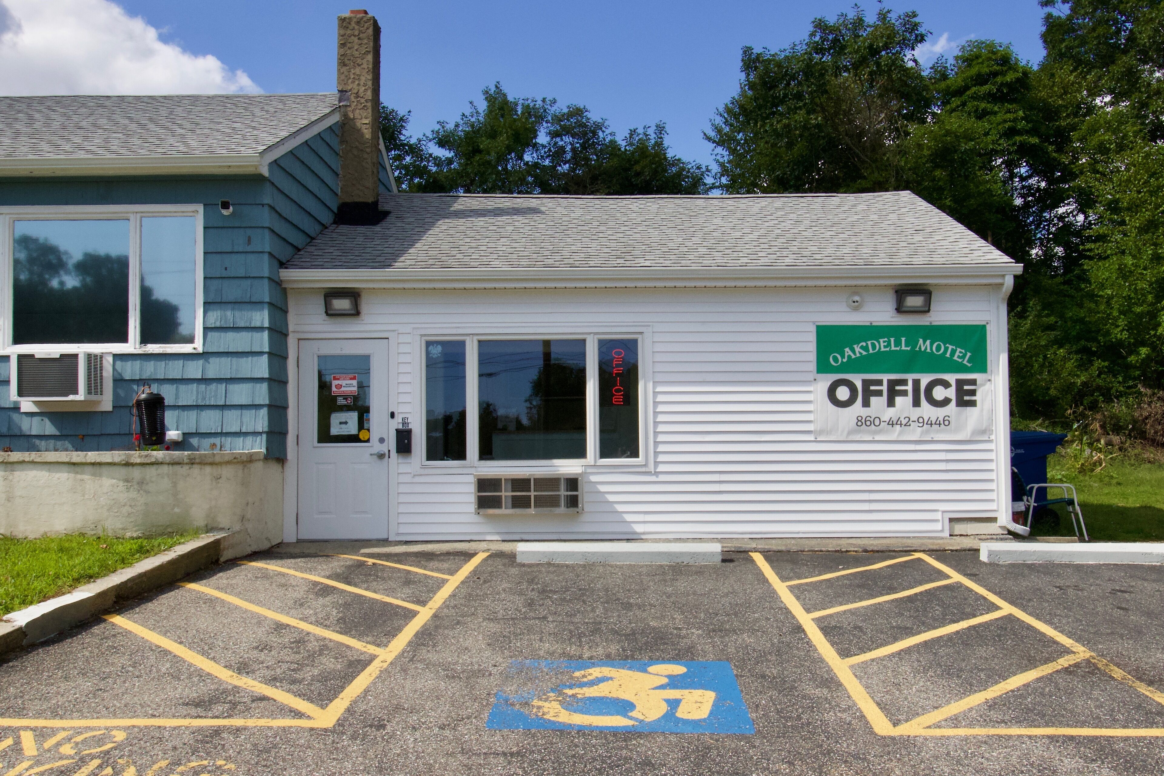 A small, single-story building with a sign reading "Oakell Motel Office" and a phone number. There are handicap parking spaces marked with a wheelchair symbol.