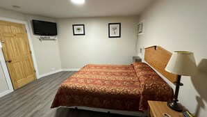 A bedroom with a bed, a bedside lamp, a telephone, a TV mounted on the wall, and two framed pictures.