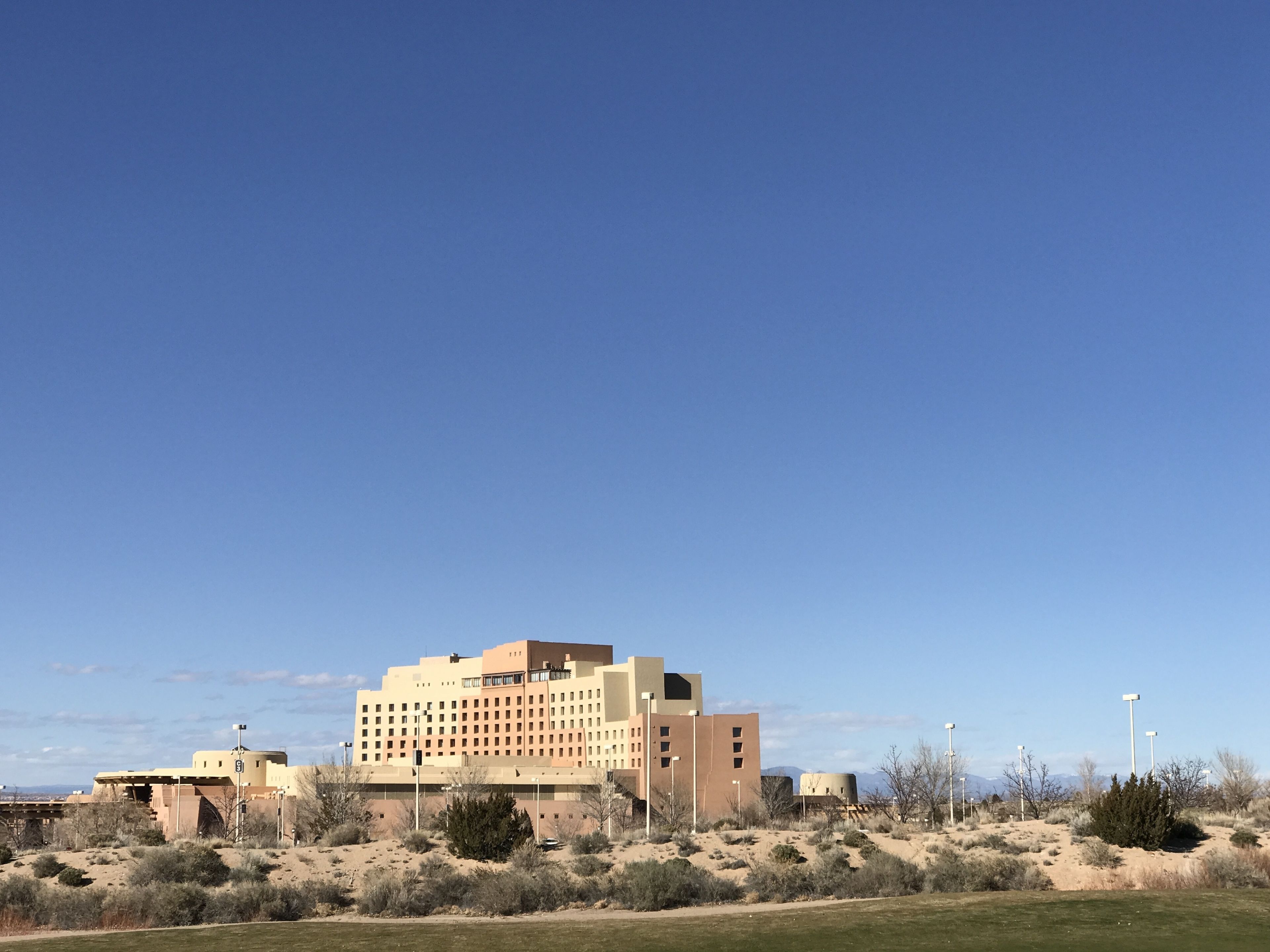 Un grand hôtel à plusieurs étages, doté d’un toit plat, entouré de végétation désertique et surplombant un ciel dégagé.