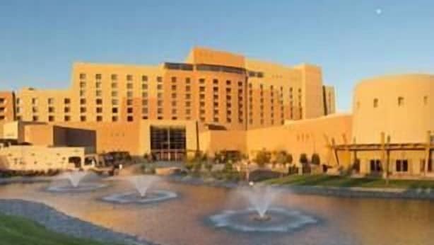 Un hotel grande con varios pisos, un patio central con fuentes y un cielo despejado.
