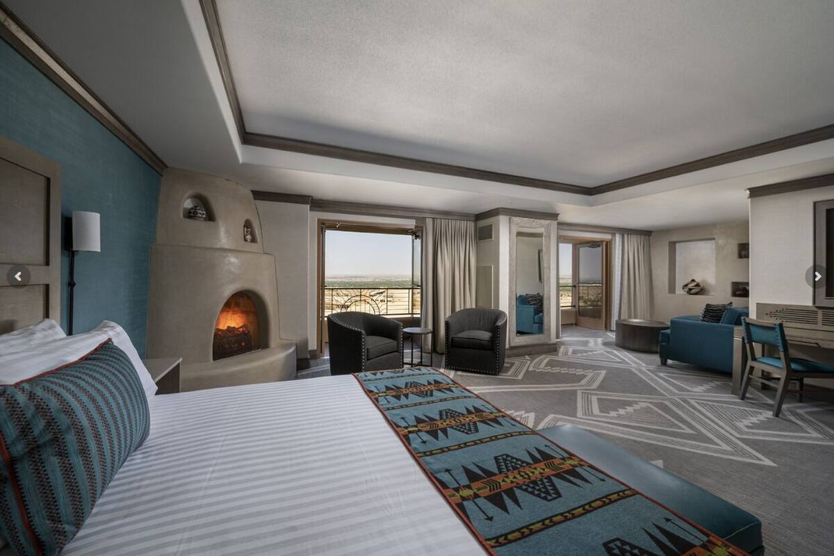 Ein Hotelzimmer mit einem großen Bett, einem Kamin, Blick auf die Wüste und einer Sitzecke mit Sesseln und einer Couch.