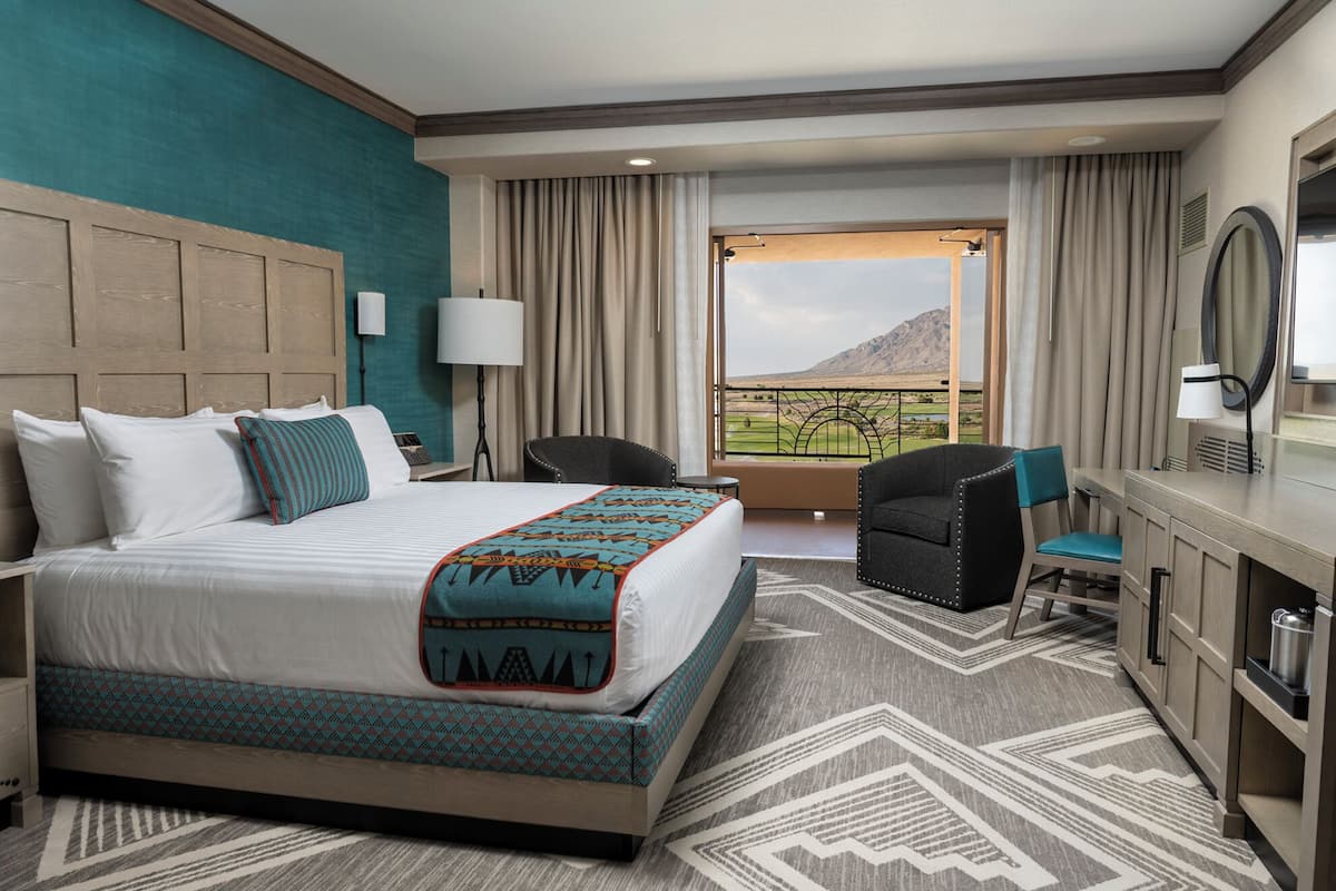 Ein Hotelzimmer mit einem großen Bett, einem Schreibtisch, einem Stuhl und Blick auf eine Berglandschaft.