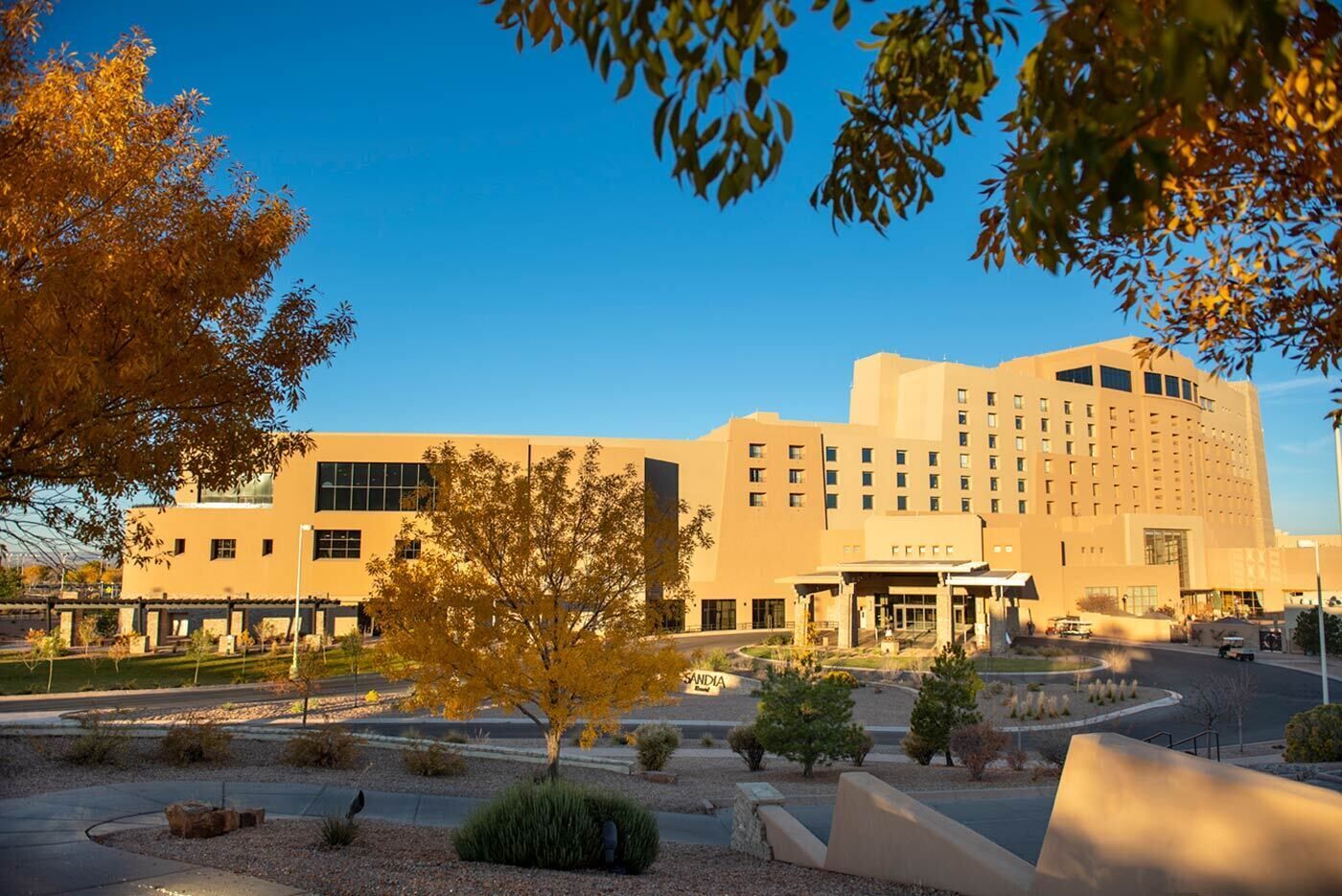A large, modern hotel with a central entrance, surrounded by landscaped gardens and trees.