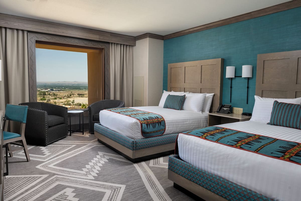 Ein Hotelzimmer mit zwei Betten, einem Schreibtisch, einem Stuhl und Blick auf die Wüstenlandschaft.