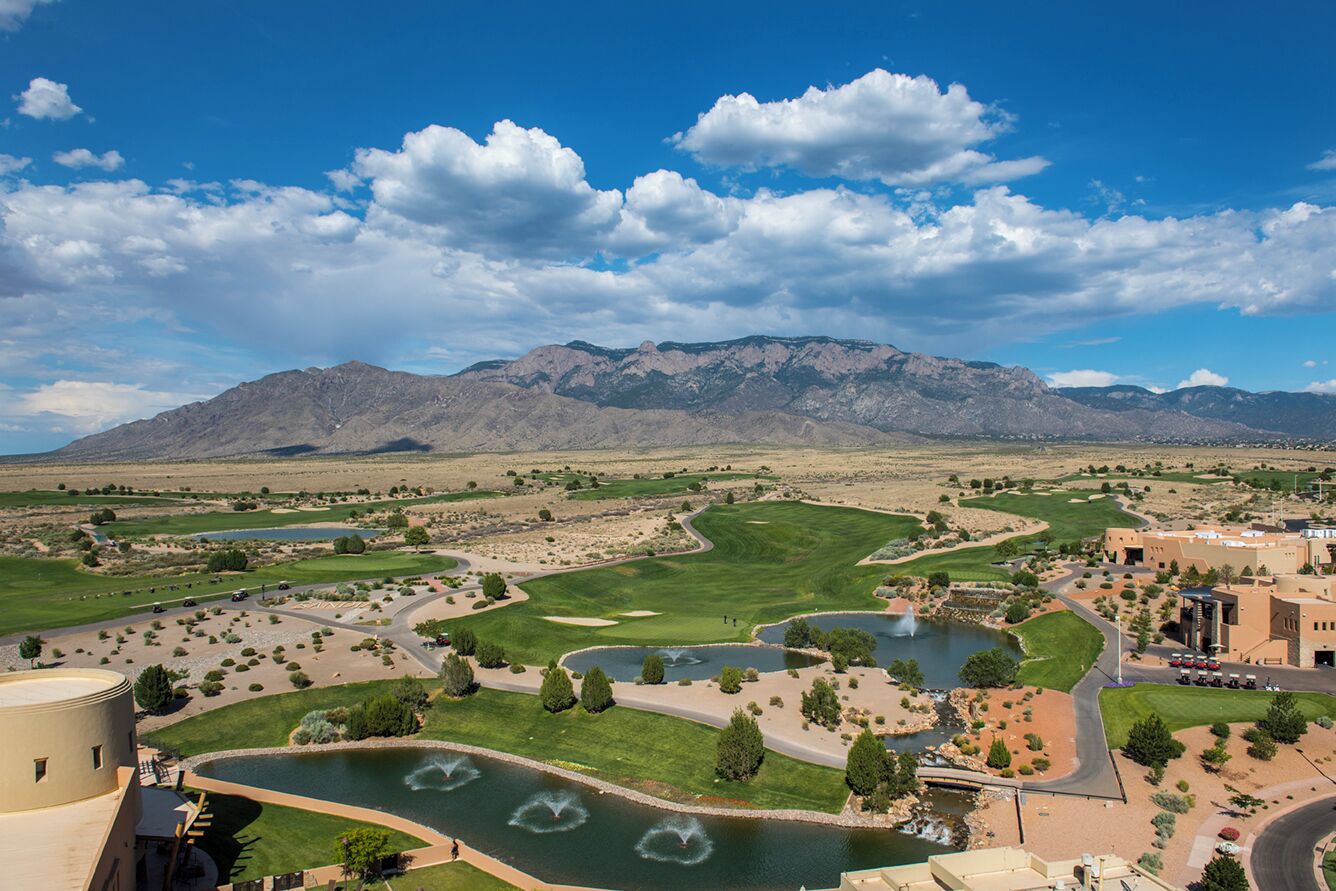 A golf course with a pond, mountains in the background, and a building with a dome structure.