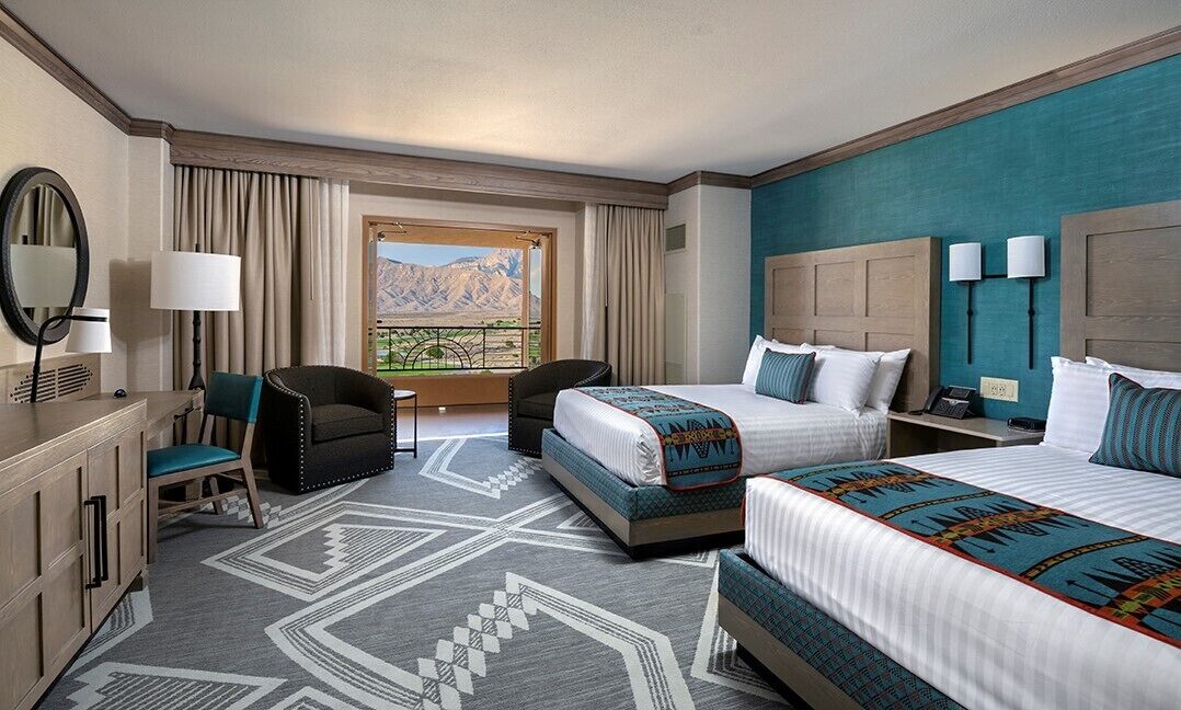 Une chambre d’hôtel avec deux lits, un bureau, une chaise, une grande fenêtre donnant sur la montagne et un tapis à motifs.