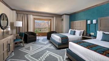 A hotel room with two beds, a desk, a chair, a large window with a mountain view, and a patterned rug.