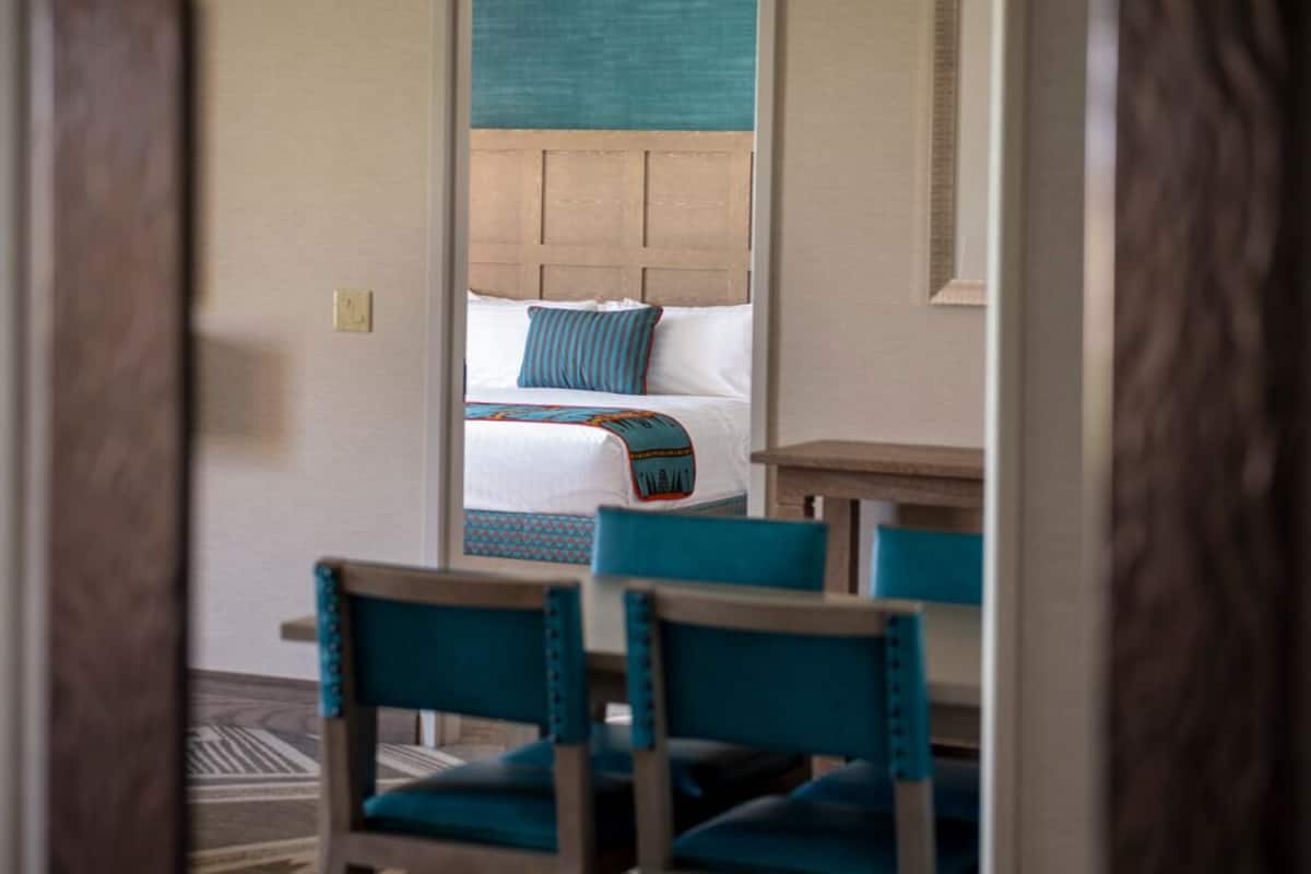 Ein Hotelzimmer mit einem Bett, einem hölzernen Kopfteil und zwei Stühlen mit Türkisbezug.