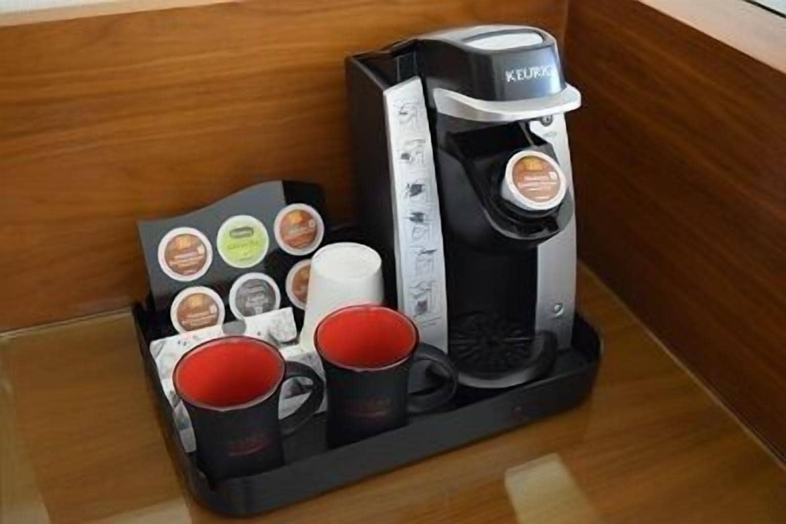 Eine Kaffeemaschine von Keurig mit einem Pod-Halter, der verschiedene Kaffeekapseln und zwei rote Tassen enthält.