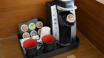 Eine Kaffeemaschine von Keurig mit einem Pod-Halter, der verschiedene Kaffeekapseln und zwei rote Tassen enthält.