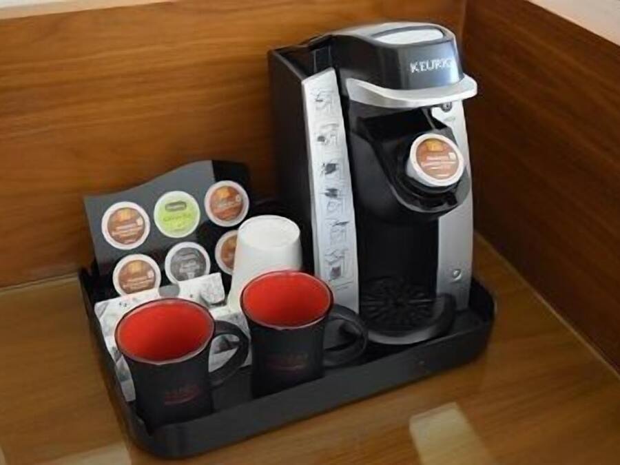 Eine Kaffeemaschine von Keurig mit einem Pod-Halter, der verschiedene Kaffeekapseln und zwei rote Tassen enthält.