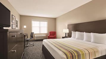 A hotel room with a large bed, a desk with a chair, a TV, and a window.