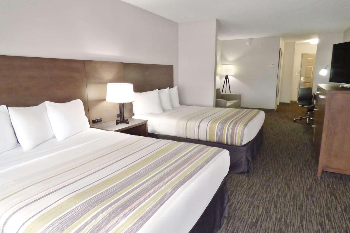 A hotel room with two beds, a desk, a lamp, a TV, and a mirror.