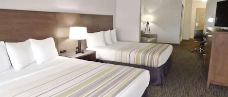 Une chambre d’hôtel avec deux lits, un bureau, une lampe, une télévision et un miroir.