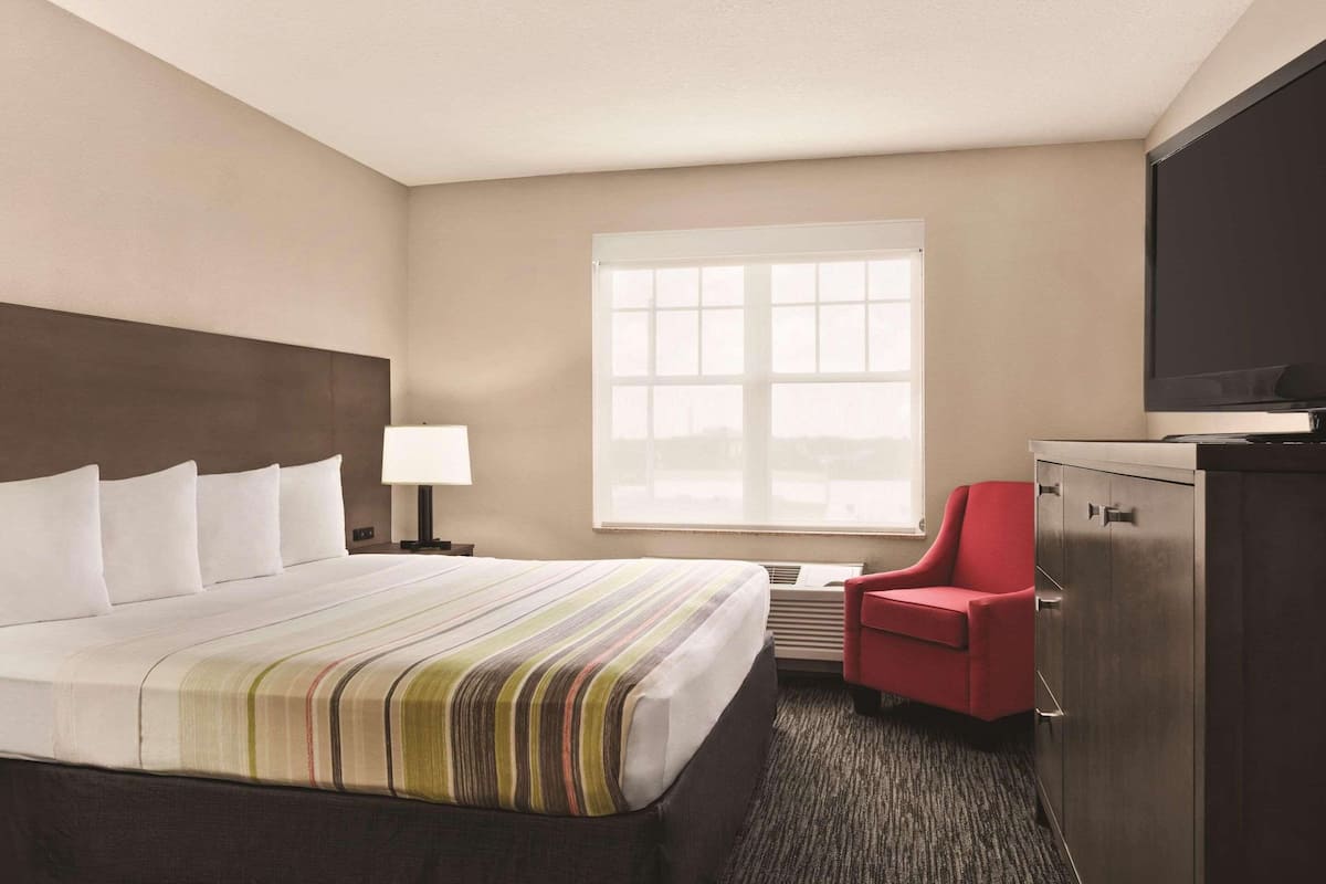 A hotel room with a large bed, a desk with a chair, a television, and a window with blinds.