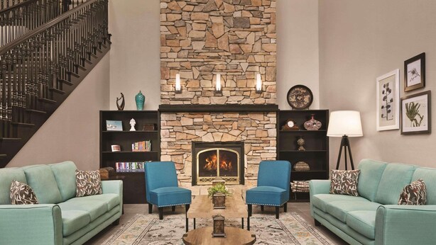 A living room with a stone fireplace, two sofas, a coffee table, and a staircase. - Country Inn & Suites by Radisson, Tampa/Brandon, FL (Tampa)