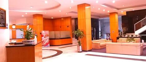 A modern lobby with a reception desk, seating area, and a staircase.