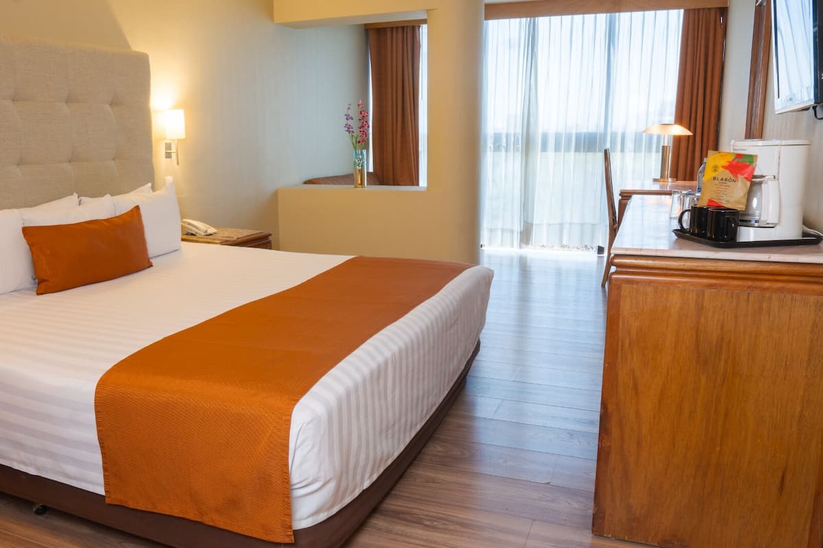 Una habitación de hotel con una cama grande, un escritorio con cafetera y una ventana con cortinas.