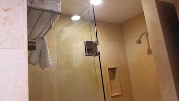 Une douche fermée par des parois en verre, avec un porte-serviettes, une pomme de douche et un petit panneau en bois sur le mur.