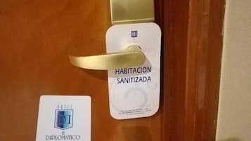 A hotel room door with a 'No Smoking' sign, a 'Sanitized Room' sign, and a 'Diplomatic' card.