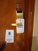 Puerta de una habitación de hotel con un cartel de 'No Fumar', un cartel de 'Habitación Sanitizada' y una tarjeta de 'Diplomático'.