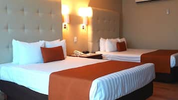 Quarto de hotel com duas camas, cada uma com roupa de cama branca e colchas laranjas. Há luminárias fixadas na parede acima das camas e um telefone na mesa de cabeceira.