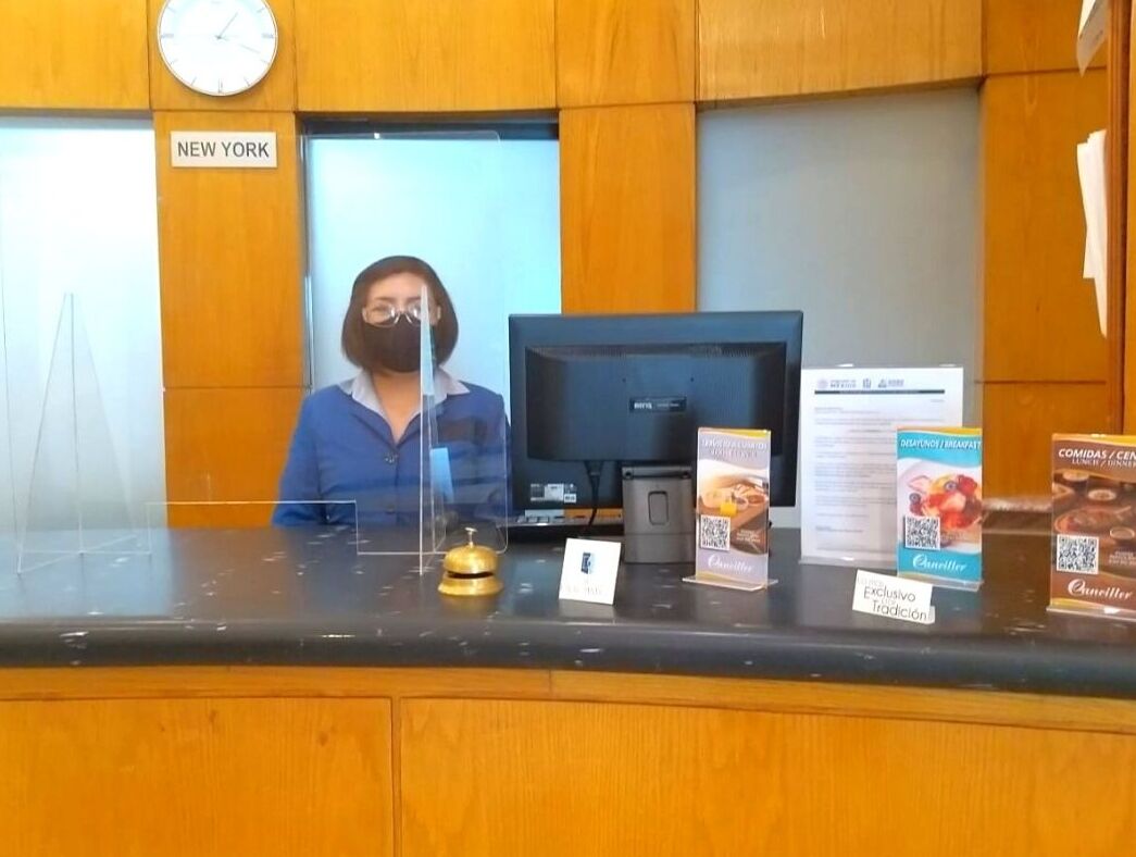 Un mostrador de recepción con un reloj, un cartel que indica 'NEW YORK' y varios folletos informativos.