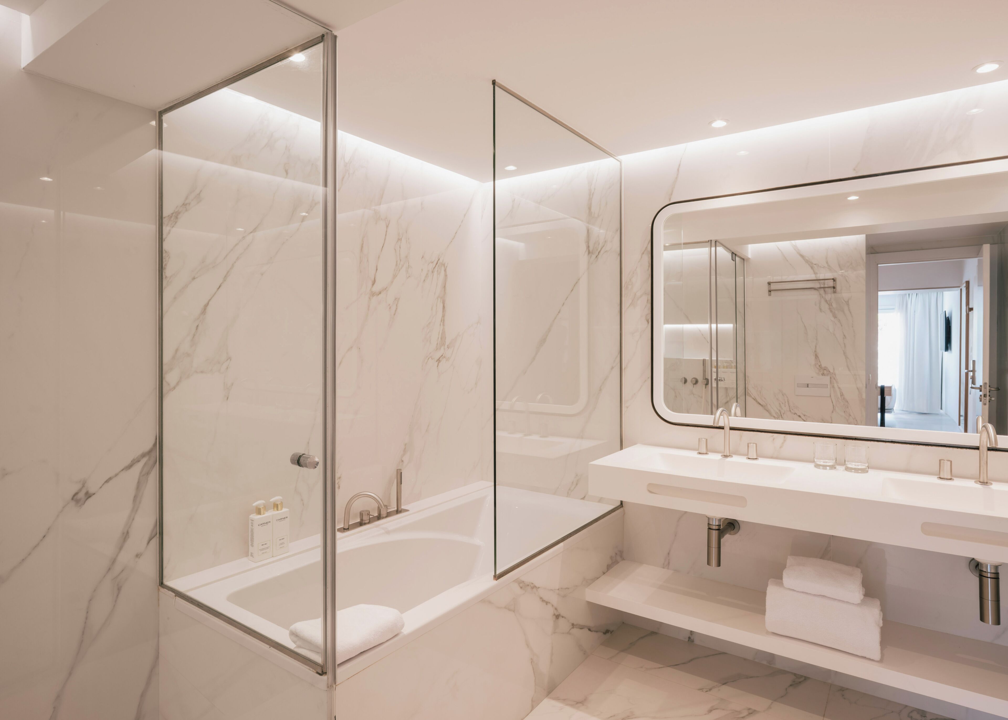 Une salle de bain moderne avec une douche à parois de verre, un grand miroir et un sol en marbre blanc.