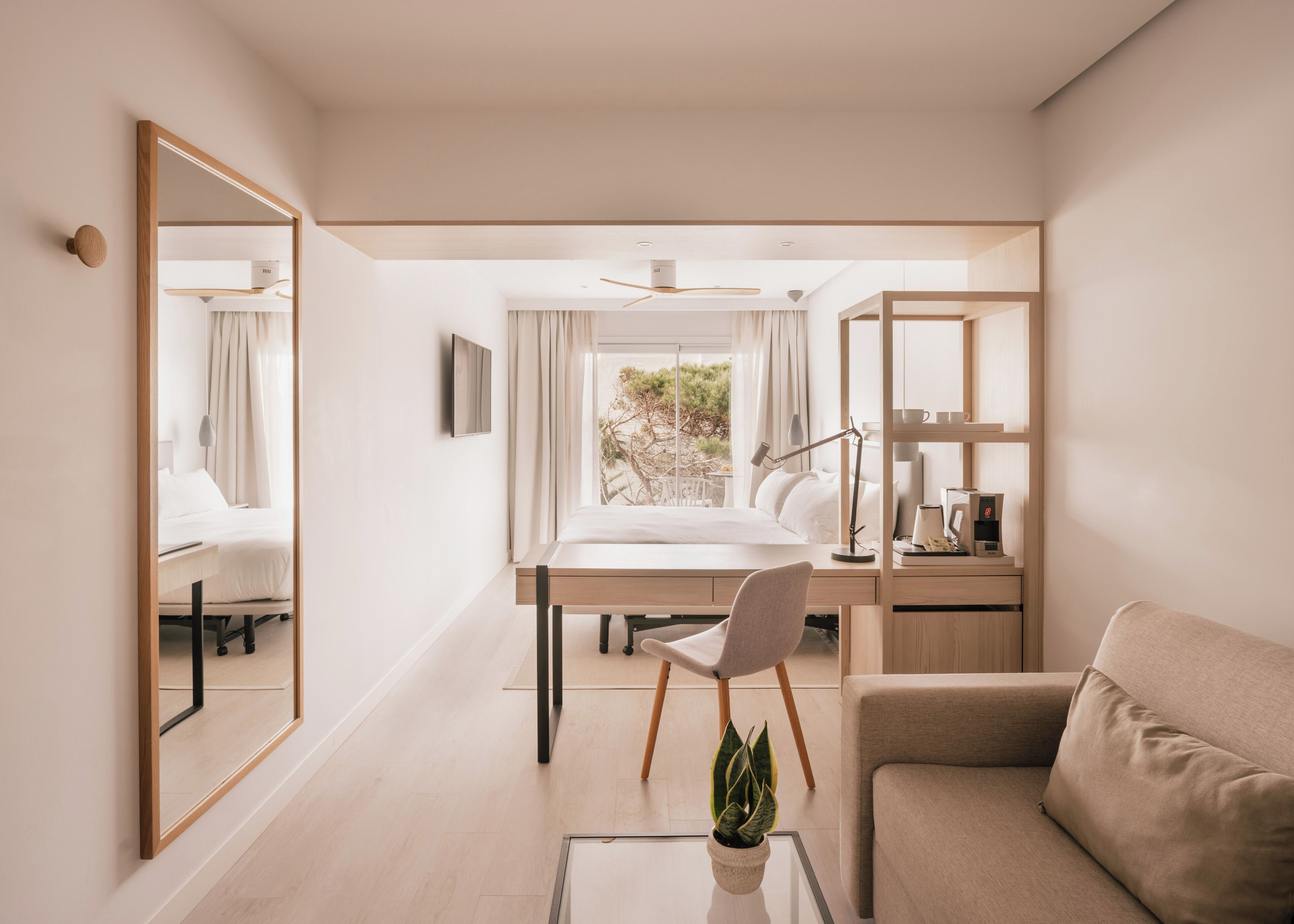 A modern hotel room with a bed, desk, chair, and a large mirror.