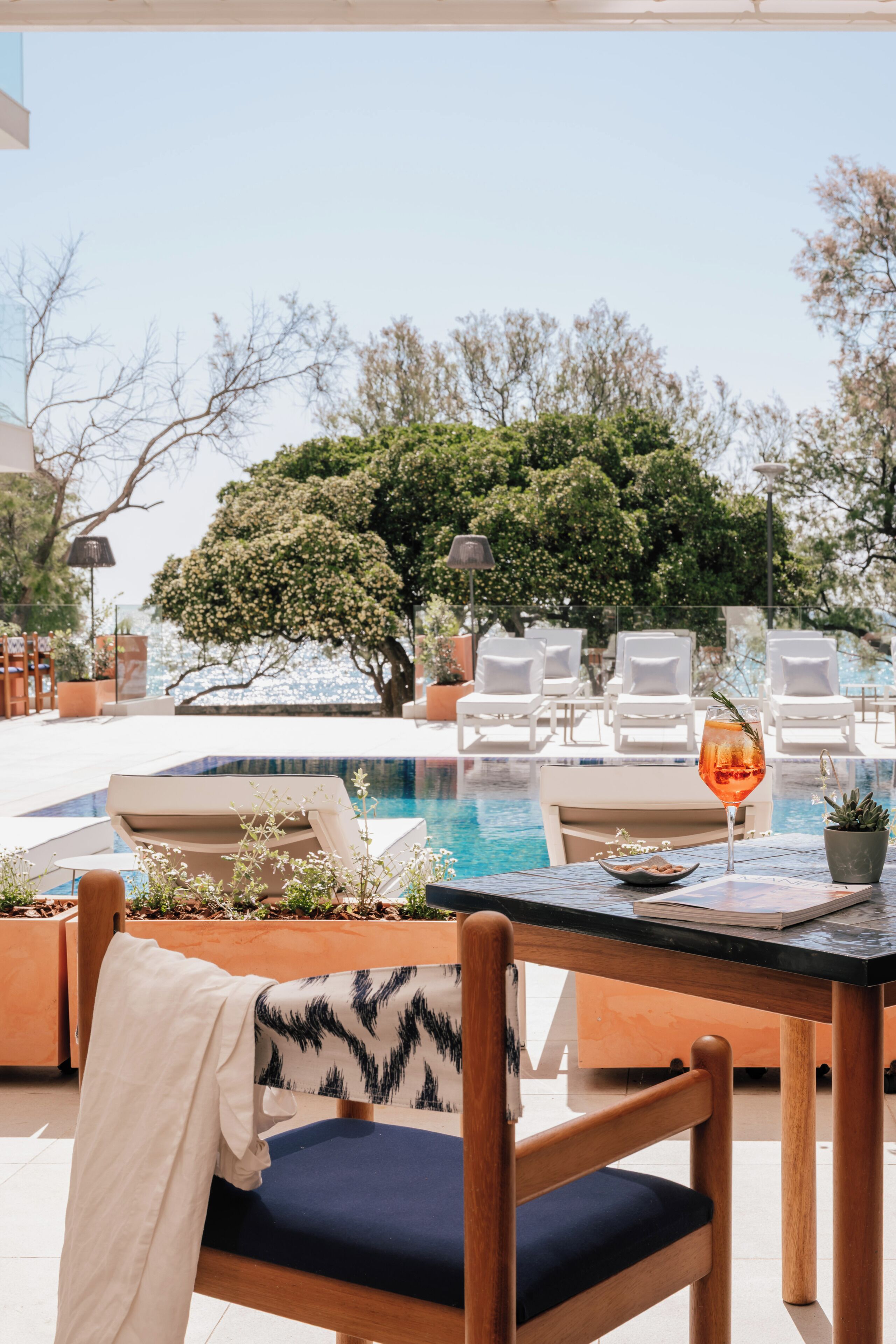 Zona de piscina con sillones, una mesa con una bebida y vista al mar.