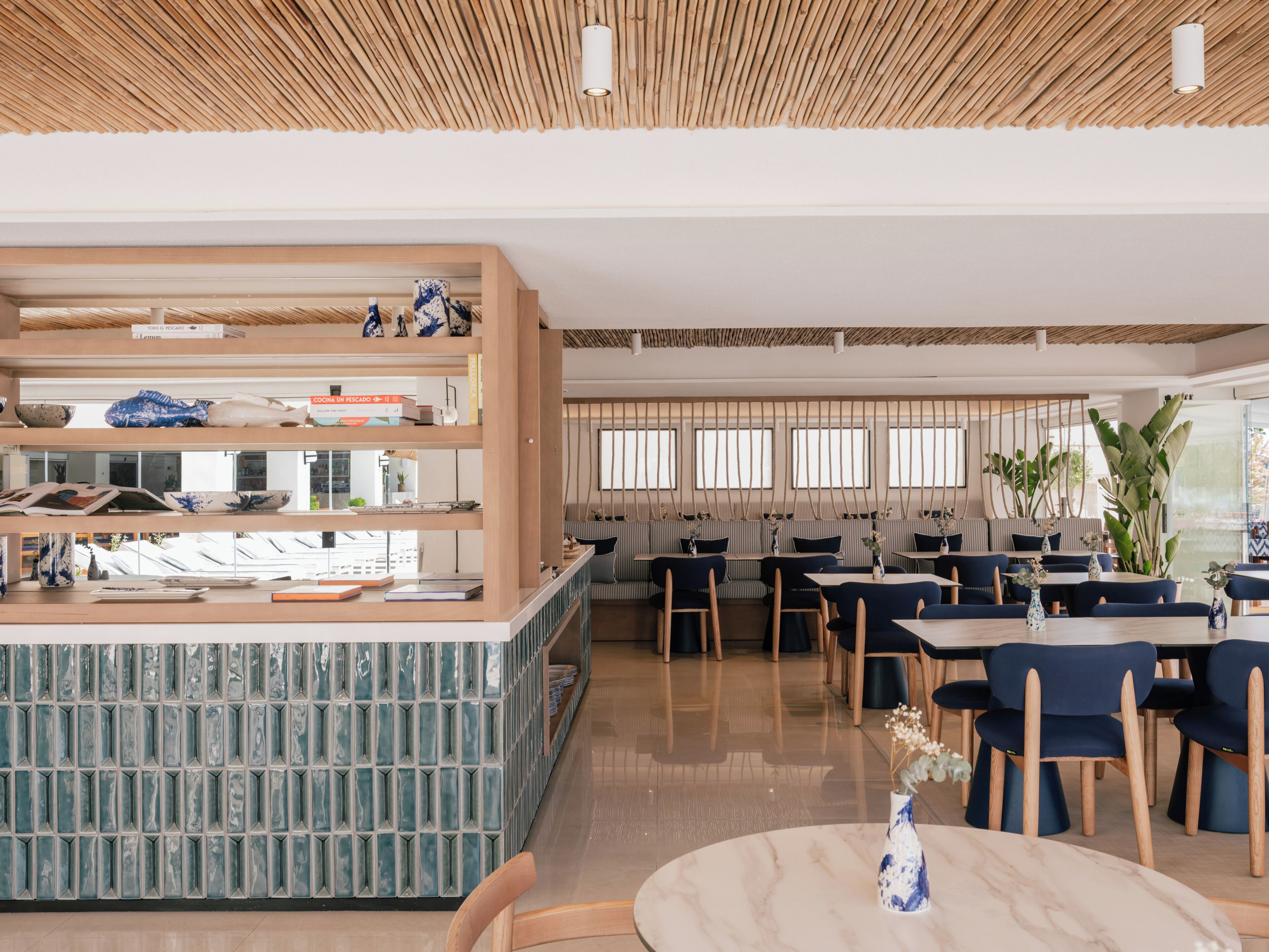 A modern restaurant interior with a central counter, seating area, and large windows.