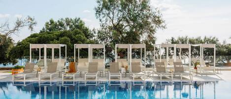 Piscina con lettini e ombrelloni, circondata da alberi.
