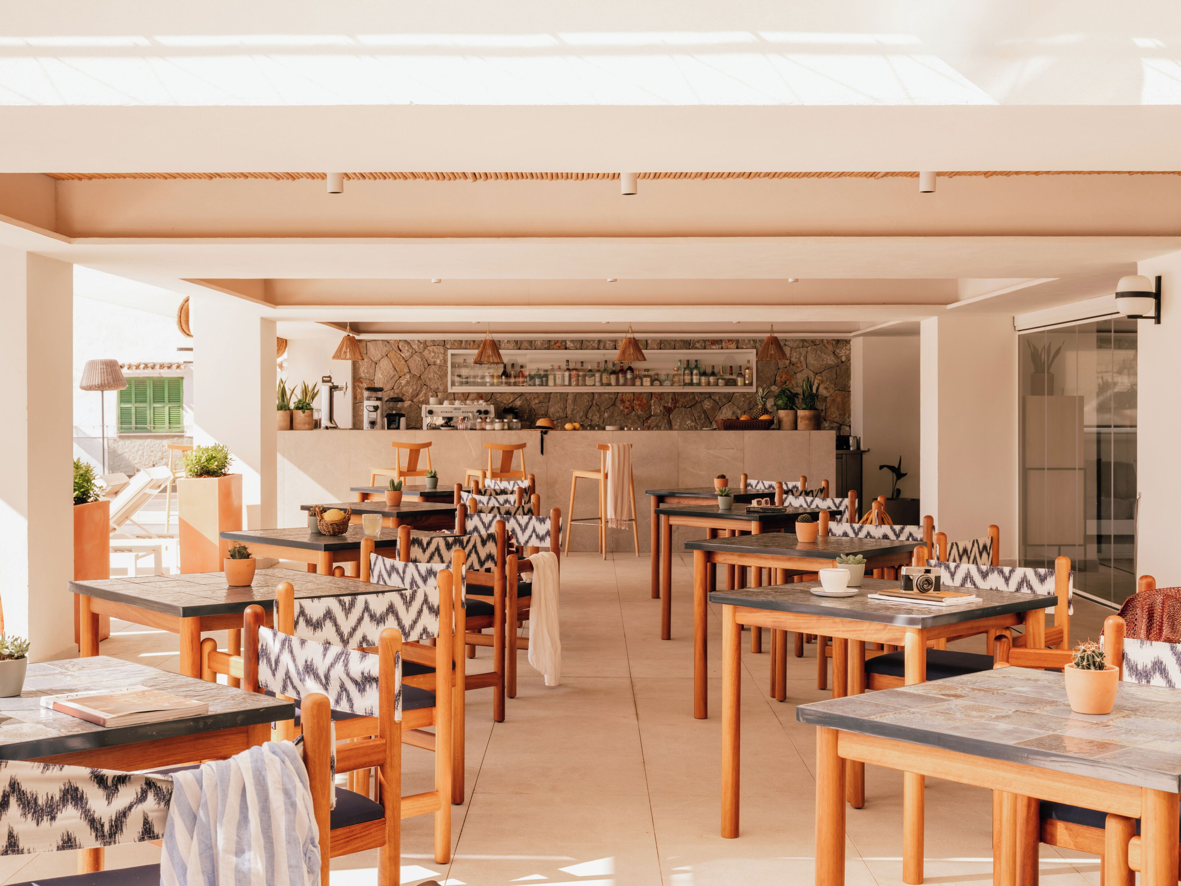 Un comedor amplio con varias mesas y sillas, una cocina al fondo y vistas al exterior.