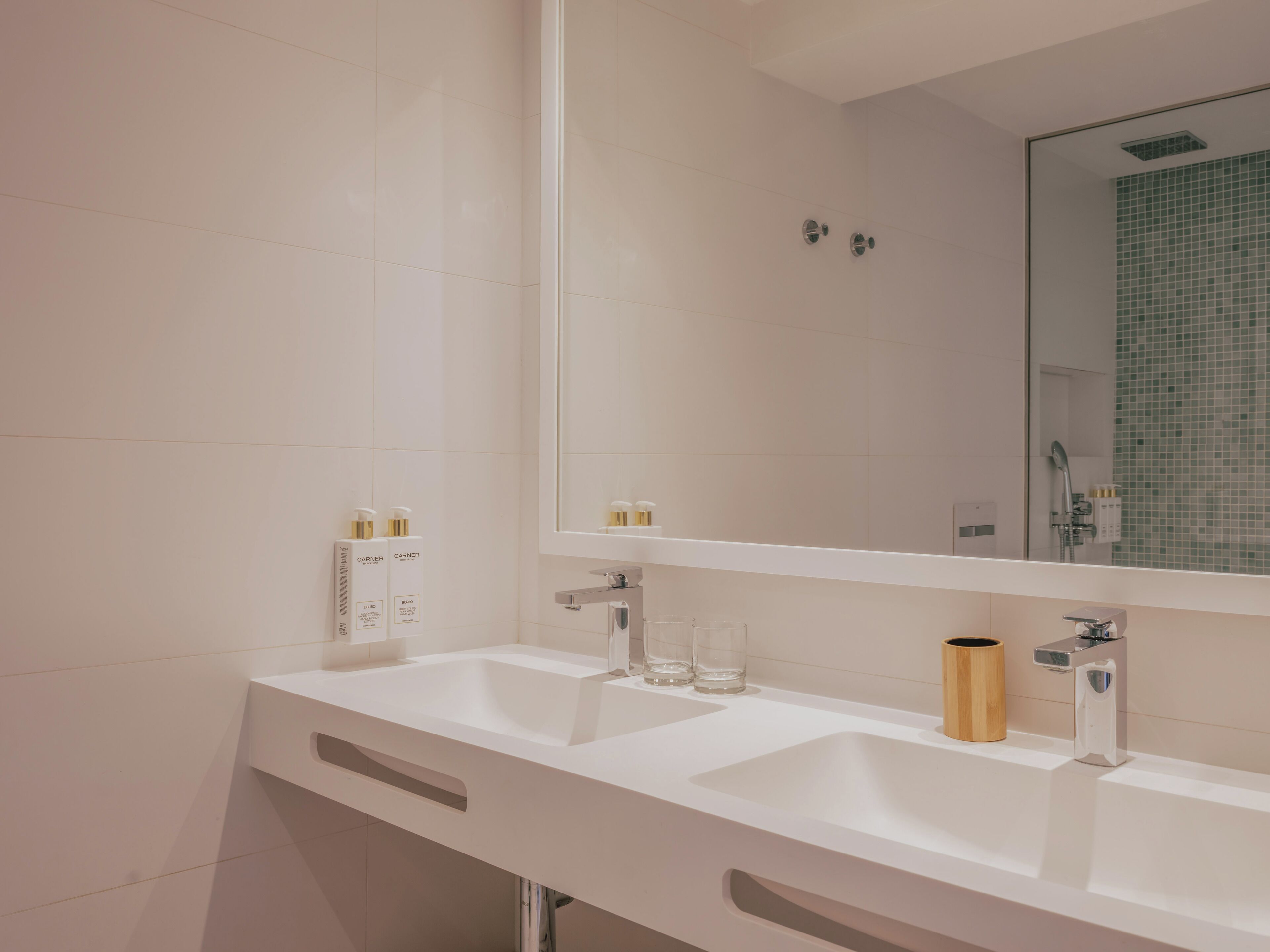 Un baño moderno con dos lavamanos, un espejo grande y una ducha con azulejos verdes.