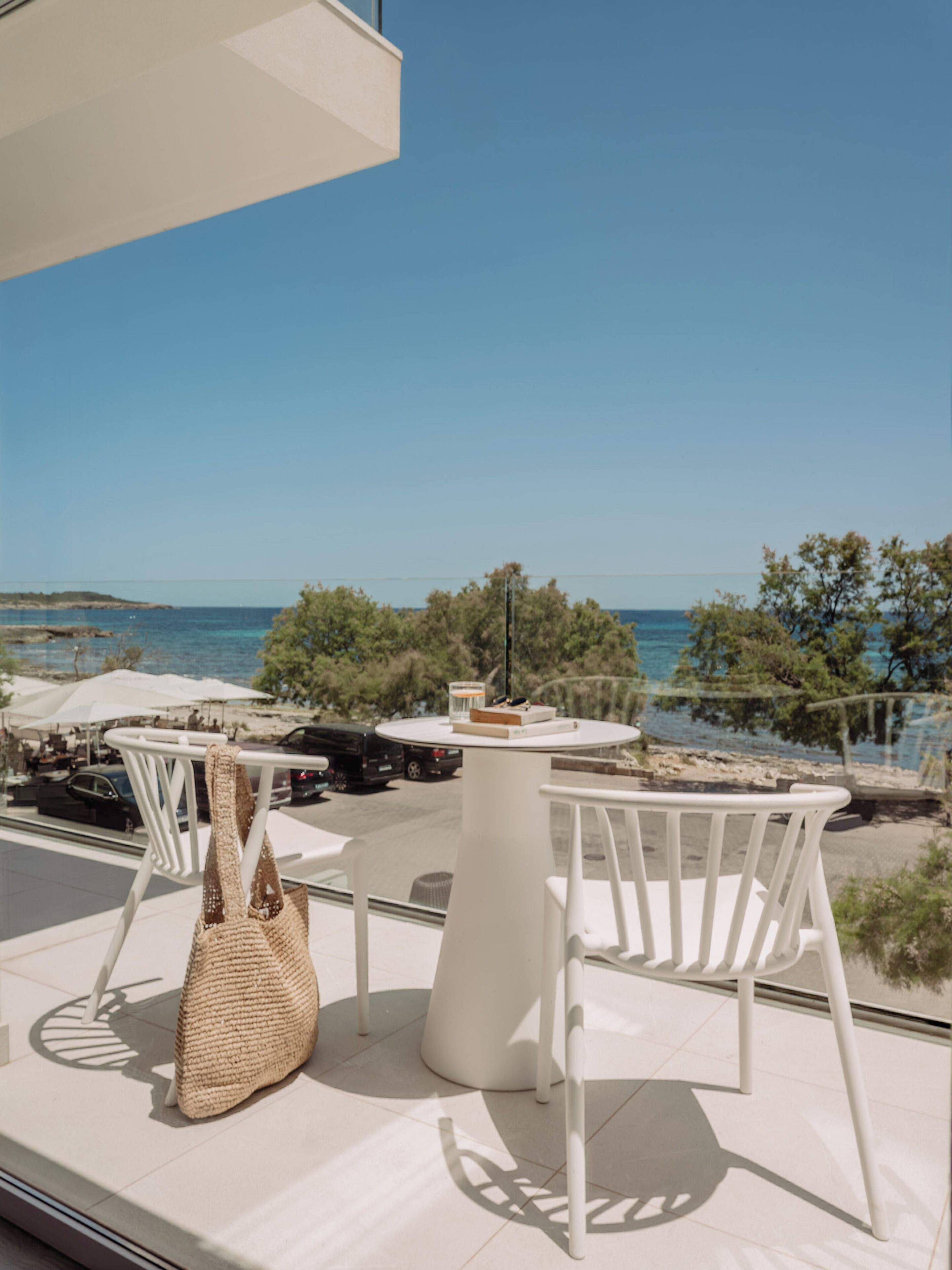 Una terraza con sillas y mesa blancas, con vista a una playa y al mar.