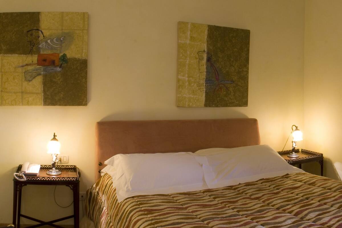 A hotel room with a bed, two bedside tables with lamps, a chair, and artwork on the walls.