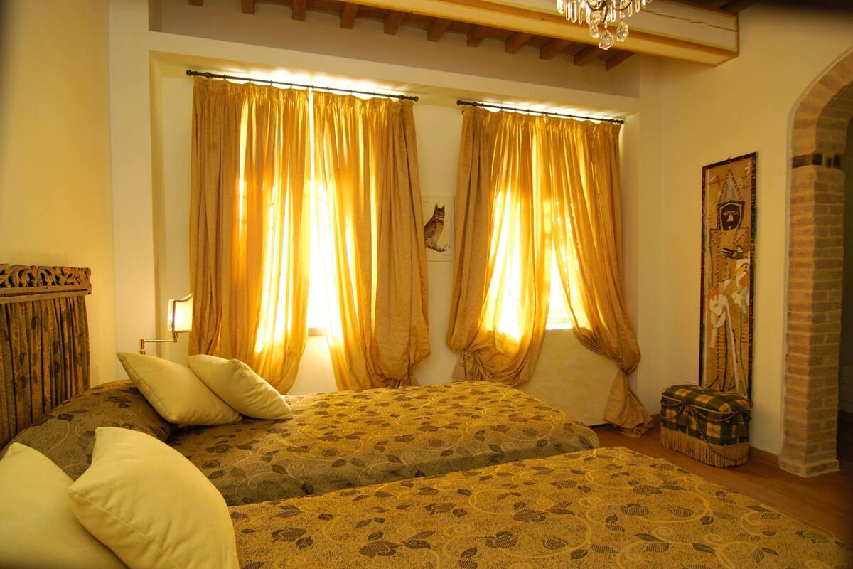 A room with two beds, a chandelier, and a cat perched on the wall.