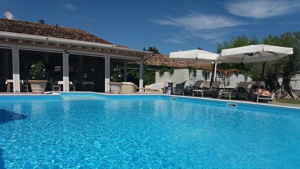 Piscina azul límpida com espreguiçadeiras e guarda-sóis, rodeada por uma área coberta com cadeiras e mesas.