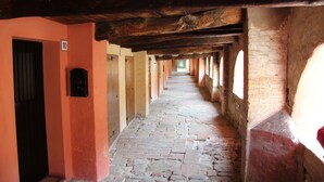 Um corredor com piso de pedra, vigas de madeira e janelas em arco.