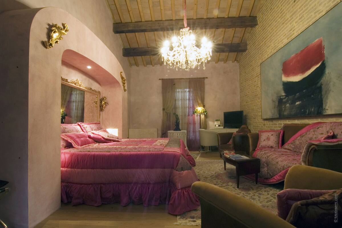 A bedroom with a large bed, a desk, and a chair. There is a chandelier hanging from the ceiling.