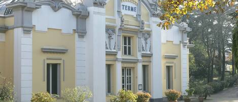 Un edificio con el nombre "TERME" en la fachada, que presenta elementos arquitectónicos clásicos y macetas con plantas en primer plano.