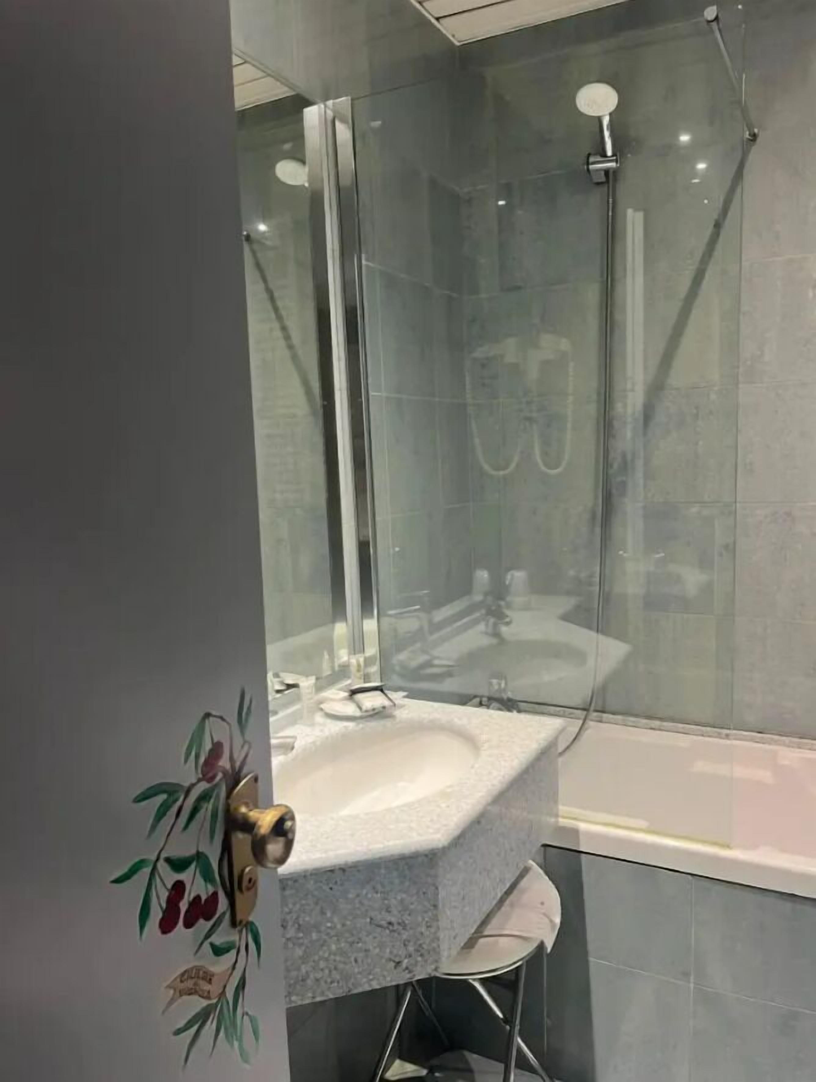A modern bathroom with a glass shower enclosure, a white sink, and a small stool.
