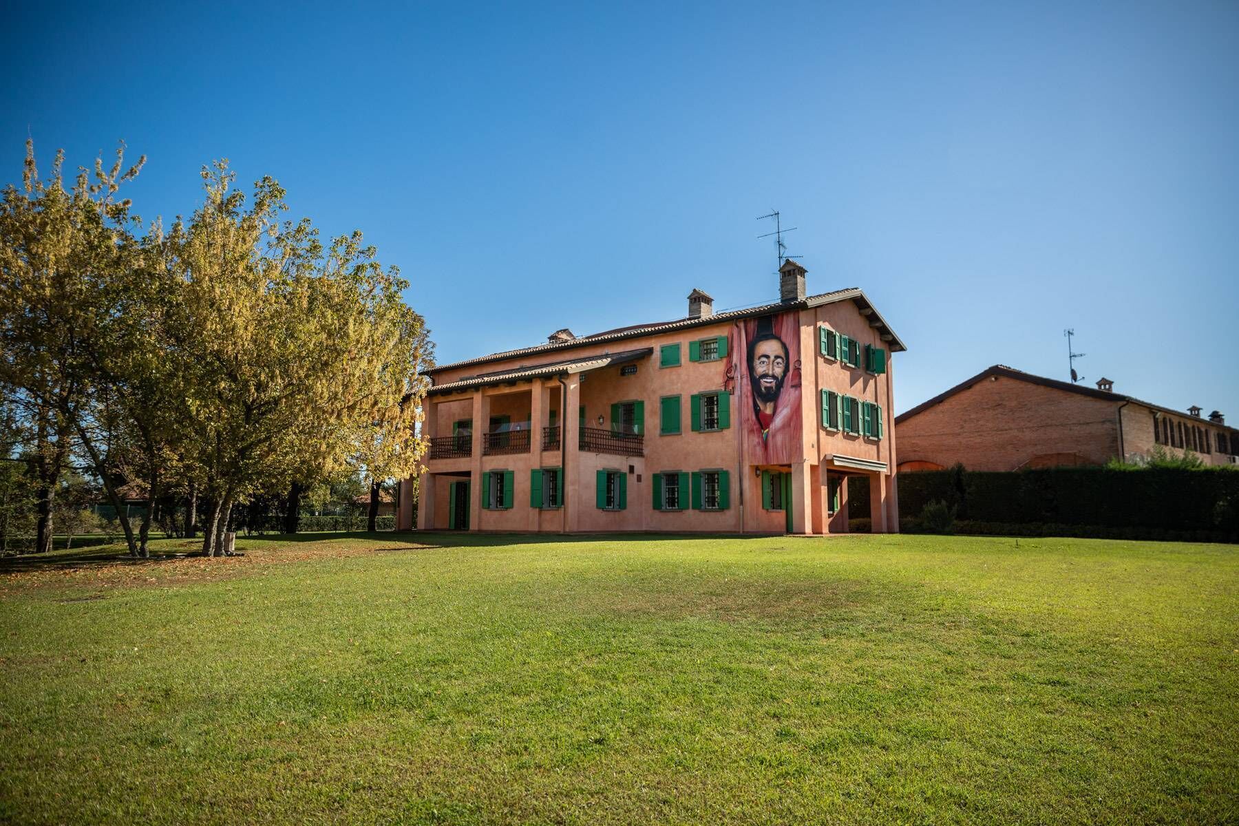 A two-story building with a large mural on the side, a grassy lawn in front, and a clear blue sky.