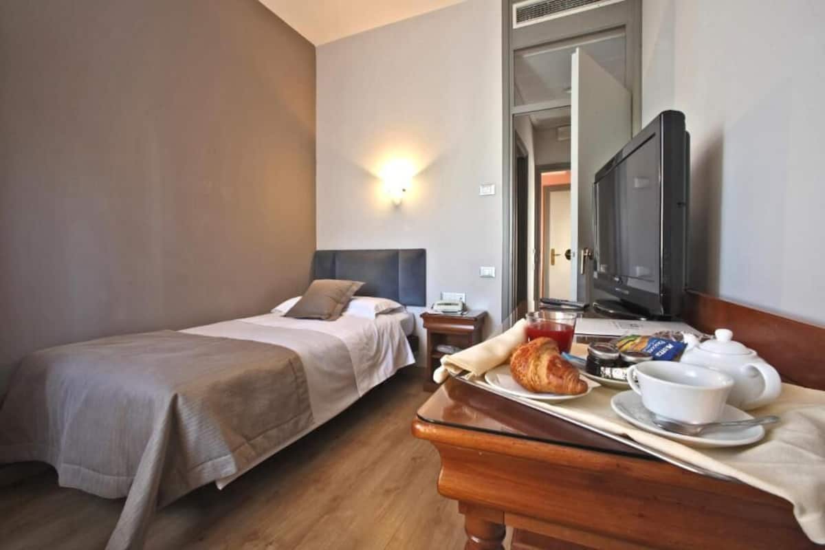 A hotel room with two beds, a TV, a breakfast tray with croissants, coffee, and tea, and a wooden nightstand.