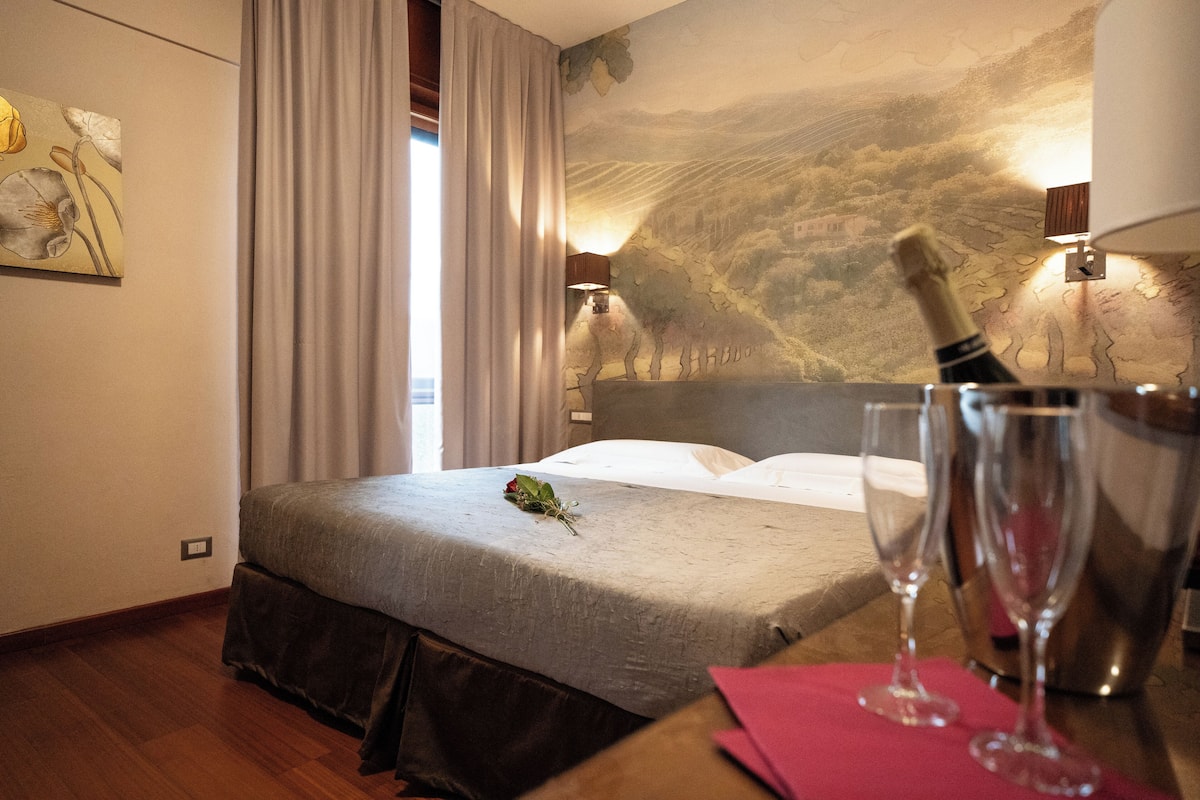 A hotel room with a bed, a bottle of champagne, and two glasses on a table.