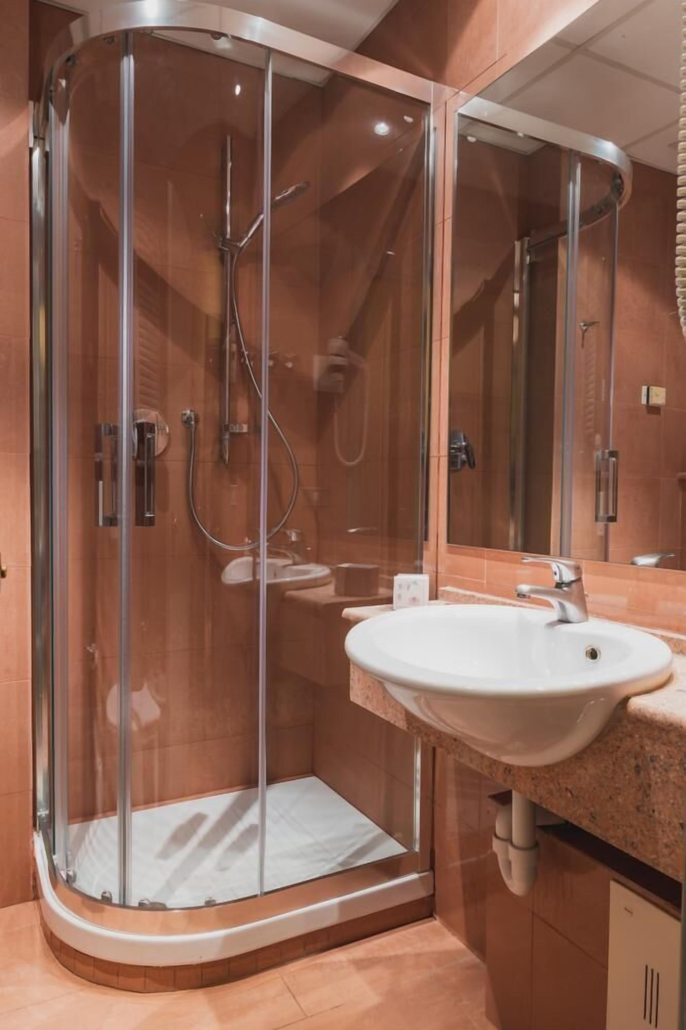 Une salle de bain moderne avec une douche à parois de verre, un lavabo blanc et un grand miroir.