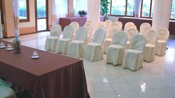 A conference room with a long table and rows of chairs, large windows, and a tiled floor.