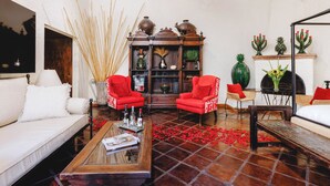 Una sala de estar con un sofá blanco, sillones rojos, una mesa de centro de madera y una chimenea decorada con cactus.